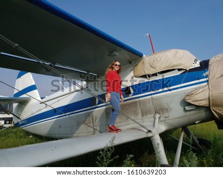 Woman portrait in front of an old aircraft. Young beautiful woman with red jacket stand in front of older bomber aircraft with a propeller in background. Photo shoot near the plane.