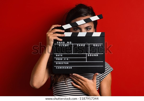 Woman portrait holding movie clapper against\
colorful red background.