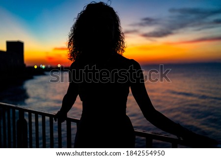 Woman portrait silhouette facing the sea at sunset. Real lifestyle image.