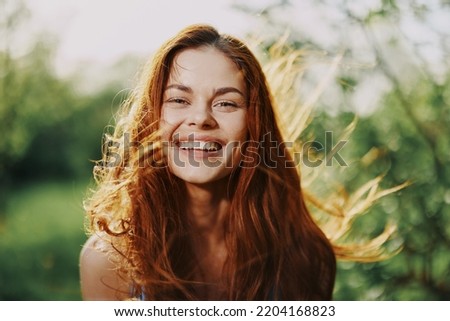 Woman portrait smile happiness catch looks into the camera with a smile with teeth spring flying hair long red, the concept of health and beauty hair sunset
