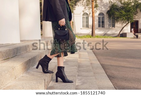 woman pose in black ankle boots with mini bag on the stairs, street style outfit