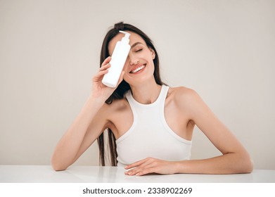 woman posing with cosmetic product in dispenser bottle on beige background. advertising concept of facial cleanser for skin care. body lotion for bodycare or professional shampoo for haircare - Shutterstock ID 2338902269