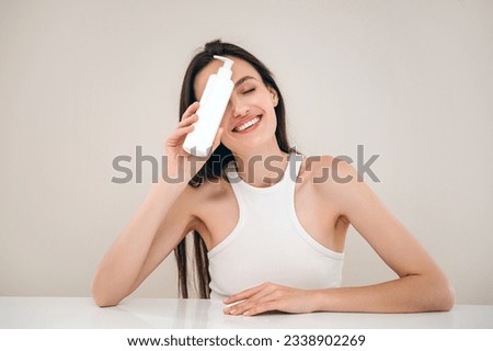 woman posing with cosmetic product in dispenser bottle on beige background. advertising concept of facial cleanser for skin care. body lotion for bodycare or professional shampoo for haircare