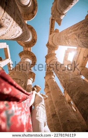 Woman posing with red scarf looking up to the sky at Karnak Temple in Luxor, Egypt