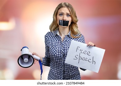 Woman Potester With Black Tape Over Mouth Standing On Red Bokeh Background.