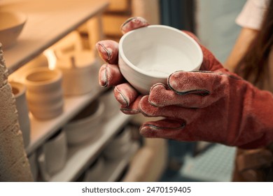 Woman potter holding clay ceramics bowl near kiln in pottery workshop - Powered by Shutterstock