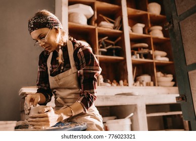 Woman potter making a clay pot on pottery wheel in workshop. Craftswoman moulding clay with her hands on pottery wheel. - Powered by Shutterstock