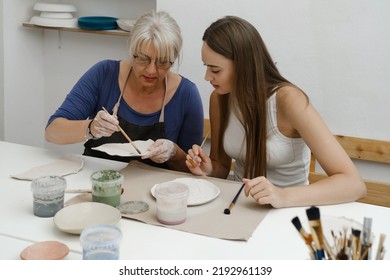 Woman potter with paintbrush glazing, painting on plate in workshop, working in pottery studio. People enjoying creative process, decorating ceramic after firing in oven. Hobby, small business - Shutterstock ID 2192961139
