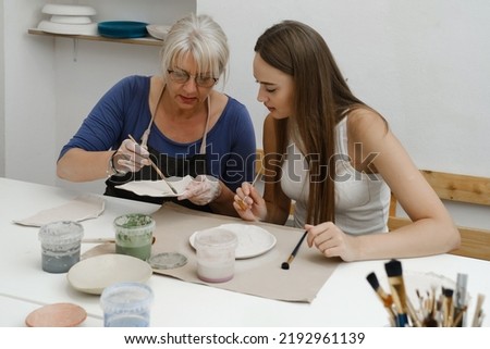 Woman potter with paintbrush glazing, painting on plate in workshop, working in pottery studio. People enjoying creative process, decorating ceramic after firing in oven. Hobby, small business
