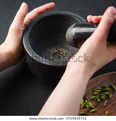 A woman pounding cardamom in a stone mortar on a dark background