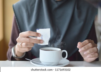 A Woman Pouring A 5g Sachet Of Sugar Into Her Cup Of Coffee