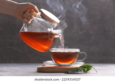 Woman pouring aromatic hot tea into glass cup on light grey table, closeup
