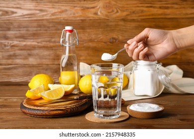 Woman Pouring Baking Soda Into Glass With Water On Wooden Background