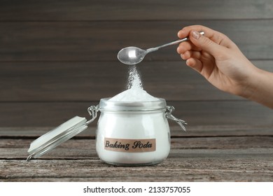 Woman Pouring Baking Soda From Spoon Into Jar At Wooden Table, Closeup