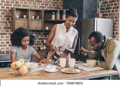 Woman pouring coffee into cups while her family is having breakfast - Powered by Shutterstock