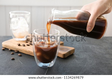 Woman pouring cold brew coffee into glass on table