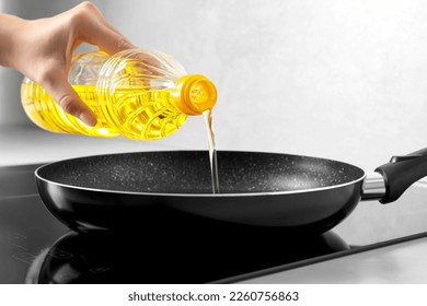 Woman pouring cooking oil from bottle into frying pan on stove, closeup