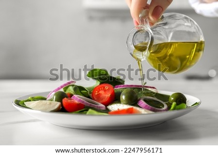 Woman pouring cooking oil onto plate with salad at white table, closeup
