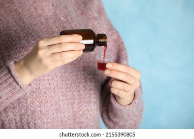 Woman pouring cough syrup into measuring cup on light blue background, closeup