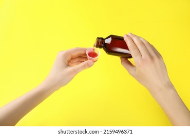 Woman pouring cough syrup into measuring cup on yellow background, closeup