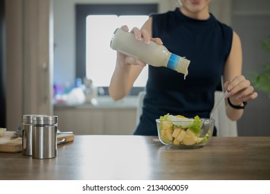 Woman Pouring Dressing Onto Healthy Vegetable Salad In Bowl.