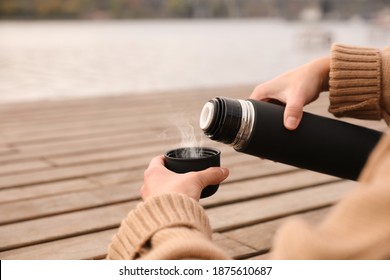 Woman pouring drink from thermos into cap at wooden table outdoors, closeup. Space for text