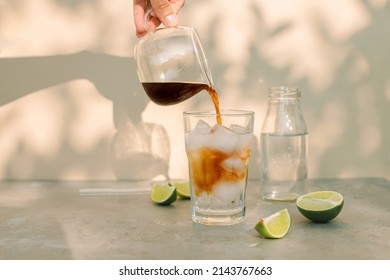 Woman pouring espresso into a glass with ice cubes and tonic. Summer refreshing menu in coffee shop.