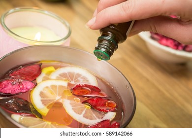 Woman pouring essential oil into a bowl for aromatherapy treatment. 