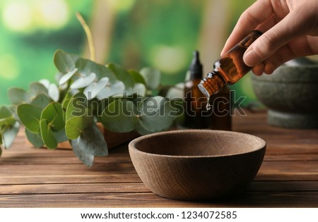 Woman pouring eucalyptus essential oil into bowl on wooden table