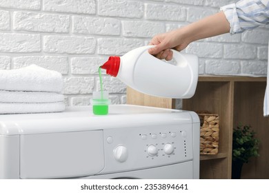 Woman pouring fabric softener from bottle into cap on washing machine indoors, closeup - Shutterstock ID 2353894641