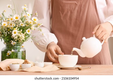 Woman Pouring Fresh Chamomile Tea From Teapot Into Cup On Table