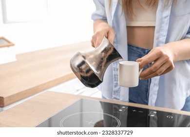 Woman pouring fresh coffee from jezve into cup in kitchen