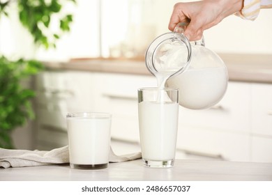 Woman pouring fresh milk from jug into glass at light wooden table in kitchen, closeup - Powered by Shutterstock