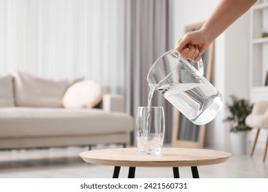 Woman pouring fresh water from jug into glass at wooden table indoors, closeup. Space for text - Powered by Shutterstock