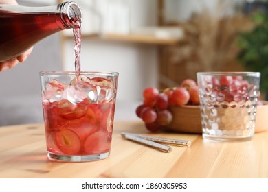 Woman Pouring Grape Soda Water Into Glass At Wooden Table Indoors, Closeup. Refreshing Drink