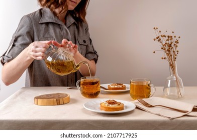 Woman pouring green herbal tea in glass cup. Hot tea is in the glass cups.Teapot and cup of tea with green tea on the table. Copy space.