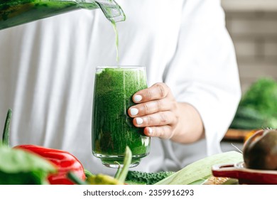 A woman pouring green smoothie to glass, healthy food concept. - Powered by Shutterstock