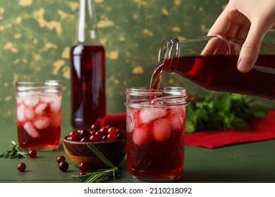 Woman pouring healthy cranberry juice from bottle into glass on color wooden background - Shutterstock ID 2110218092