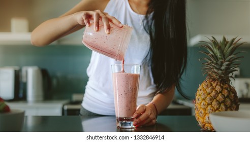 Woman pouring healthy smoothie in glass from grinder jar on kitchen counter. Female preparing fresh fruit smoothie in her kitchen with pineapple on the counter. - Powered by Shutterstock