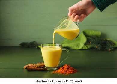 Woman Pouring Healthy Turmeric Latte From Jug Into Cup On Table