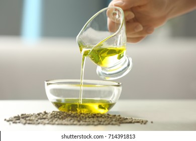 Woman pouring hemp oil in glass bowl on blurred background