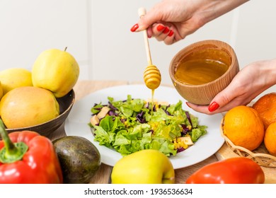 Woman pouring honey mustard dressing into bowl with fresh salad on table
