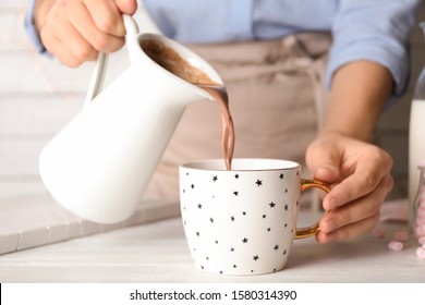 Woman Pouring Hot Cocoa Drink Into Cup On White Wooden Table, Closeup