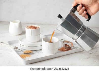 Woman pouring hot coffee from pot into cup on table