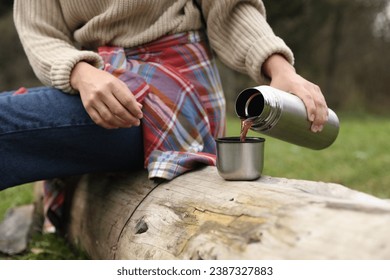 Woman pouring hot drink from metallic thermos into cup lid outdoors, closeup - Powered by Shutterstock