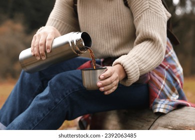 Woman pouring hot drink from metallic thermos into cup lid outdoors, closeup