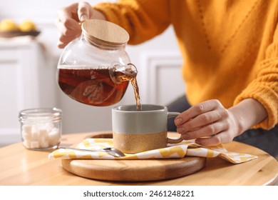 Woman pouring hot tea into cup at wooden table, closeup - Powered by Shutterstock