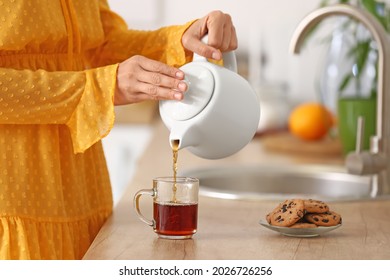 Woman pouring hot tea from teapot into cup in kitchen - Powered by Shutterstock