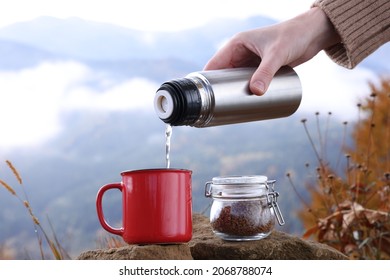 Woman Pouring Hot Water From Thermos Into Mug With Instant Coffee In Mountains, Closeup