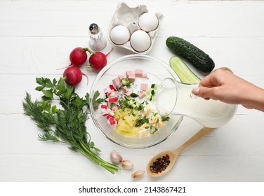 Woman Pouring Kefir Into Bowl With Ingredients For Okroshka On White Wooden Background